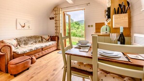 A cozy room with a sofa, a dining table with chairs, a kitchen area with utensils, and a view of greenery outside.