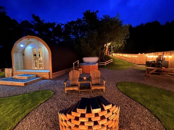 A cozy outdoor area with a wooden structure, seating, and a hot tub.