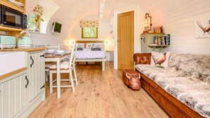 A compact room with a kitchenette, a bed with a headboard, a sofa, and a small table with chairs.