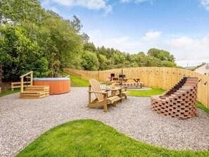 A backyard with a hot tub, wooden deck, and a brick fire pit.