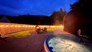 A hot tub with a wooden deck, a fire pit, and a wooden fence with lights.