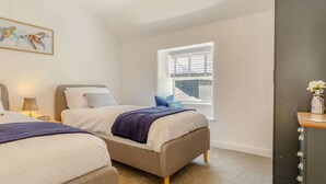 Quarto com duas camas, uma janela com persianas, uma mesa de cabeceira com abajur e um armário.
