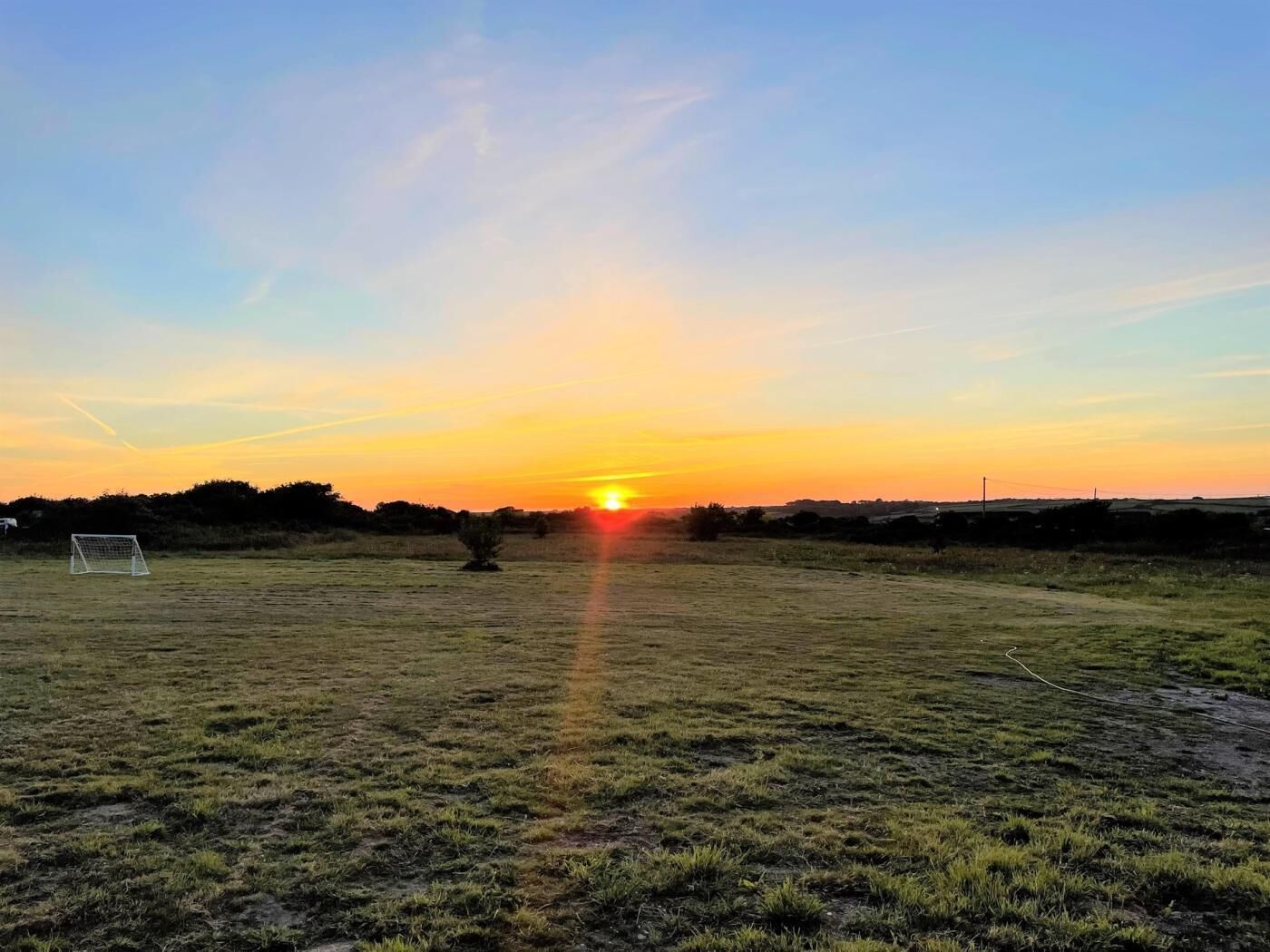 Een veld met een doelpunt, een kleine boom en een ondergaande zon op de achtergrond.
