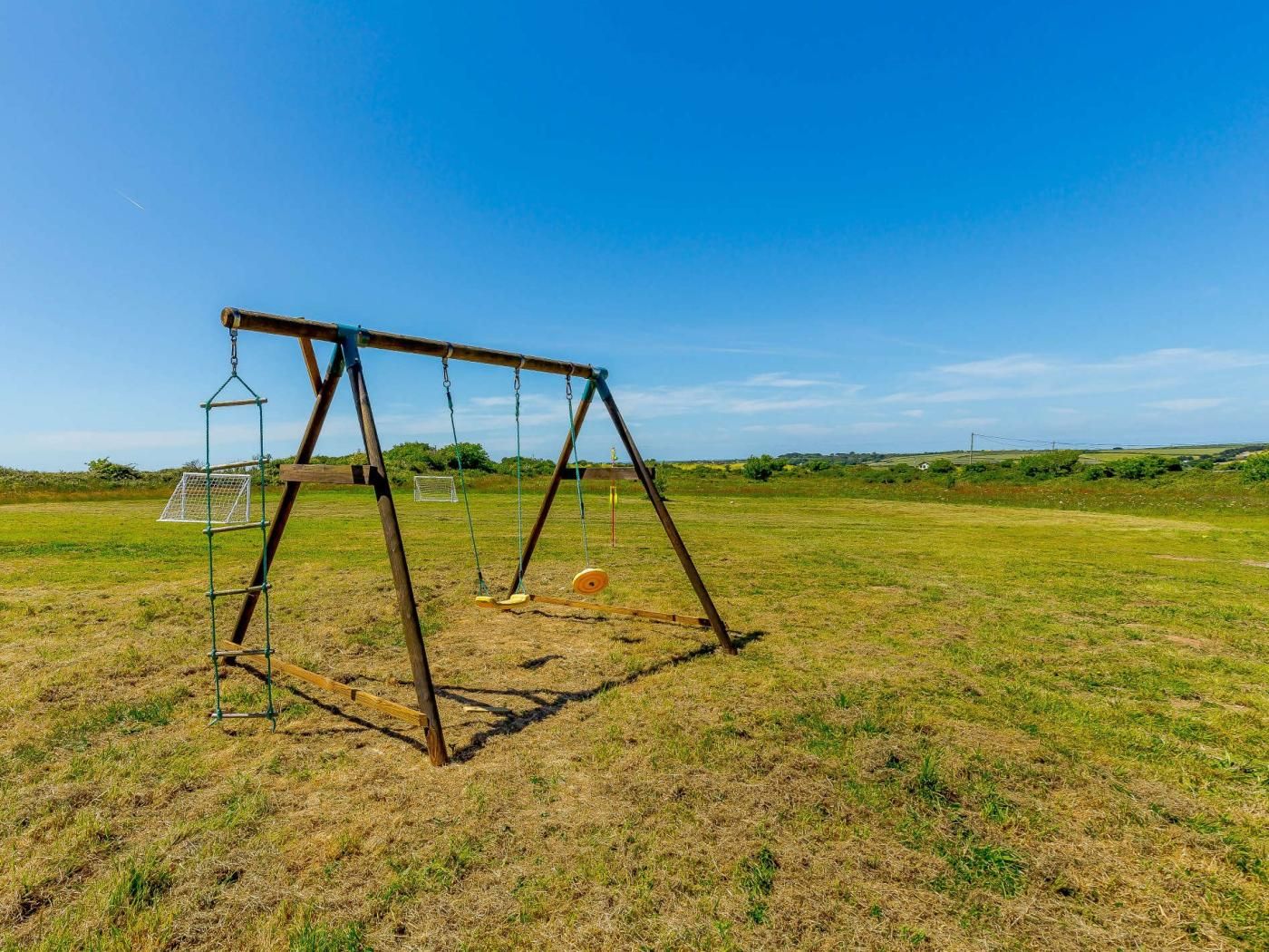 Une balançoire en bois installée dans un champ dégagé, sous un ciel clair.