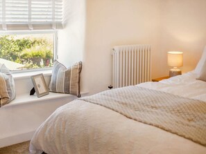 A bedroom with a large bed, a bedside table with a lamp, a radiator, and a window with blinds. - 3 Bed in Redruth (oc-88102) (Redruth)