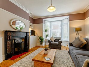Ein Wohnzimmer mit Kamin, einer Couch, einem Couchtisch und einem großen Fenster mit Jalousien.
