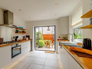 Eine moderne Küche mit einer zentralen Kochinsel, einem eingebauten Backofen und einer Schiebetür zu einer Terrasse.