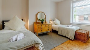 Une chambre avec deux lits simples, une commode en bois, un miroir, un luminaire suspendu et une fenêtre avec des stores.