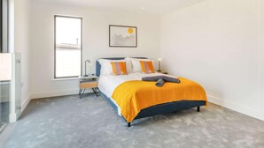 Une chambre à coucher moderne avec un lit, une table de chevet, une fenêtre et un tableau au mur.