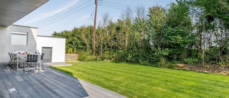 A modern outdoor patio with a wooden deck, a dining table, and chairs.