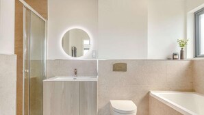 Une salle de bain moderne avec une douche à parois de verre, un miroir rond, un lavabo et des toilettes.