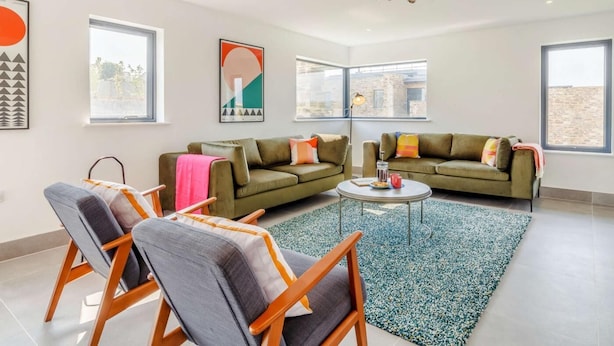 Un salon moderne avec un canapé vert, deux fauteuils, une table basse et des œuvres d’art accrochées aux murs.