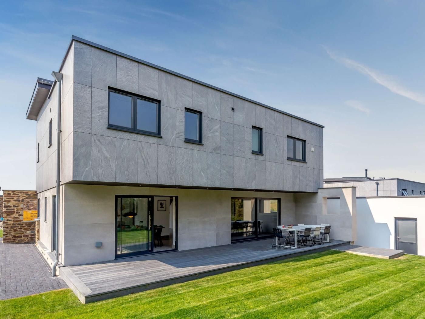A modern two-story house with a flat roof, large windows, and a covered patio area.