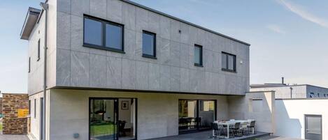 Une maison moderne à deux étages, dotée d’un toit plat, de grandes fenêtres et d’un patio couvert.