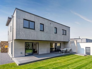 Ein modernes, zweistöckiges Haus mit Flachdach, großen Fenstern und einer überdachten Terrasse.