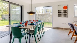 Un coin repas avec une table dressée pour six personnes, des chaises vertes et une suspension.