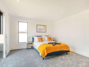 Ein modernes Schlafzimmer mit Bett, Nachttisch, Fenster und einem Bild an der Wand.