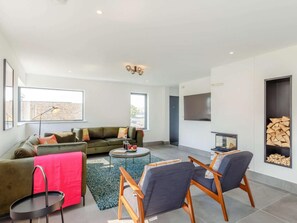 A modern living room with a sofa, chairs, a coffee table, and a fireplace. - 4 Bed in Bude (oc-88965) (Widemouth Bay)
