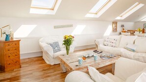 Ein geräumiges Schlafzimmer im Loft-Stil mit Dachfenstern, einer Holzkommode, einem weißen Sofa und einem Couchtisch.
