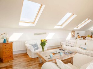 Ein geräumiges Schlafzimmer im Loft-Stil mit Dachfenstern, einer Holzkommode, einem weißen Sofa und einem Couchtisch.