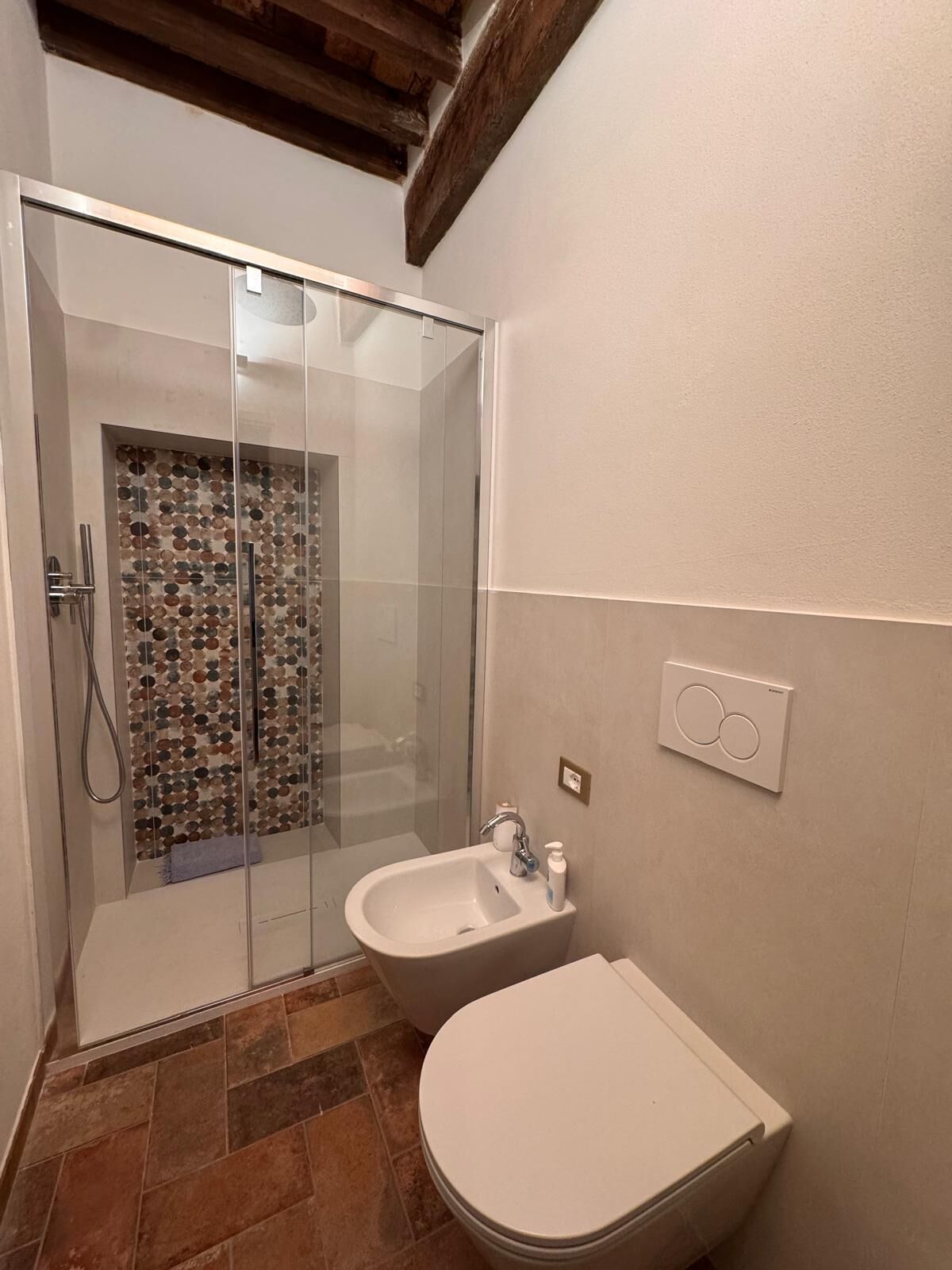 Un baño con mampara de vidrio, lavamanos blanco y un inodoro.
