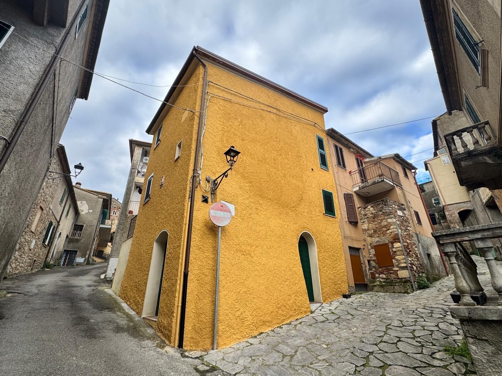 Une rue étroite avec un bâtiment jaune, des murs en pierre et un chemin pavé.