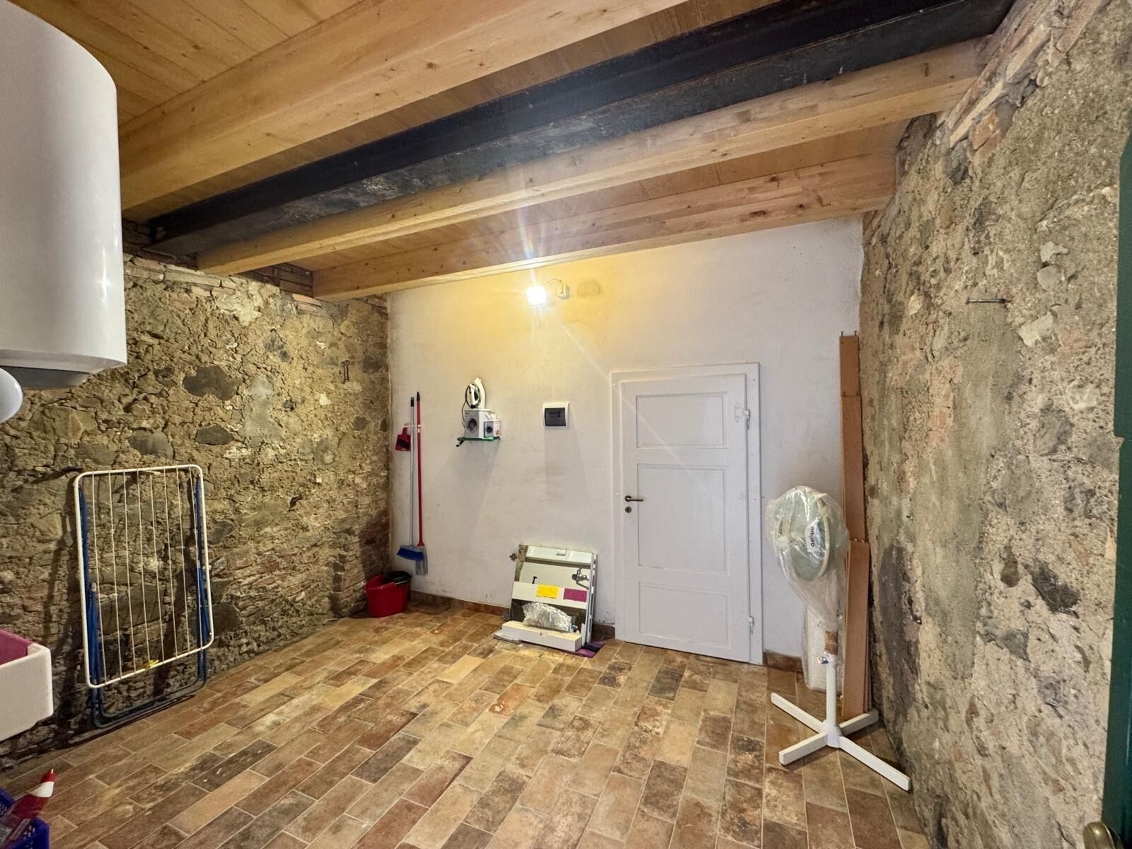 Una habitación rústica con pared de piedra, puerta blanca y suelo de baldosas.