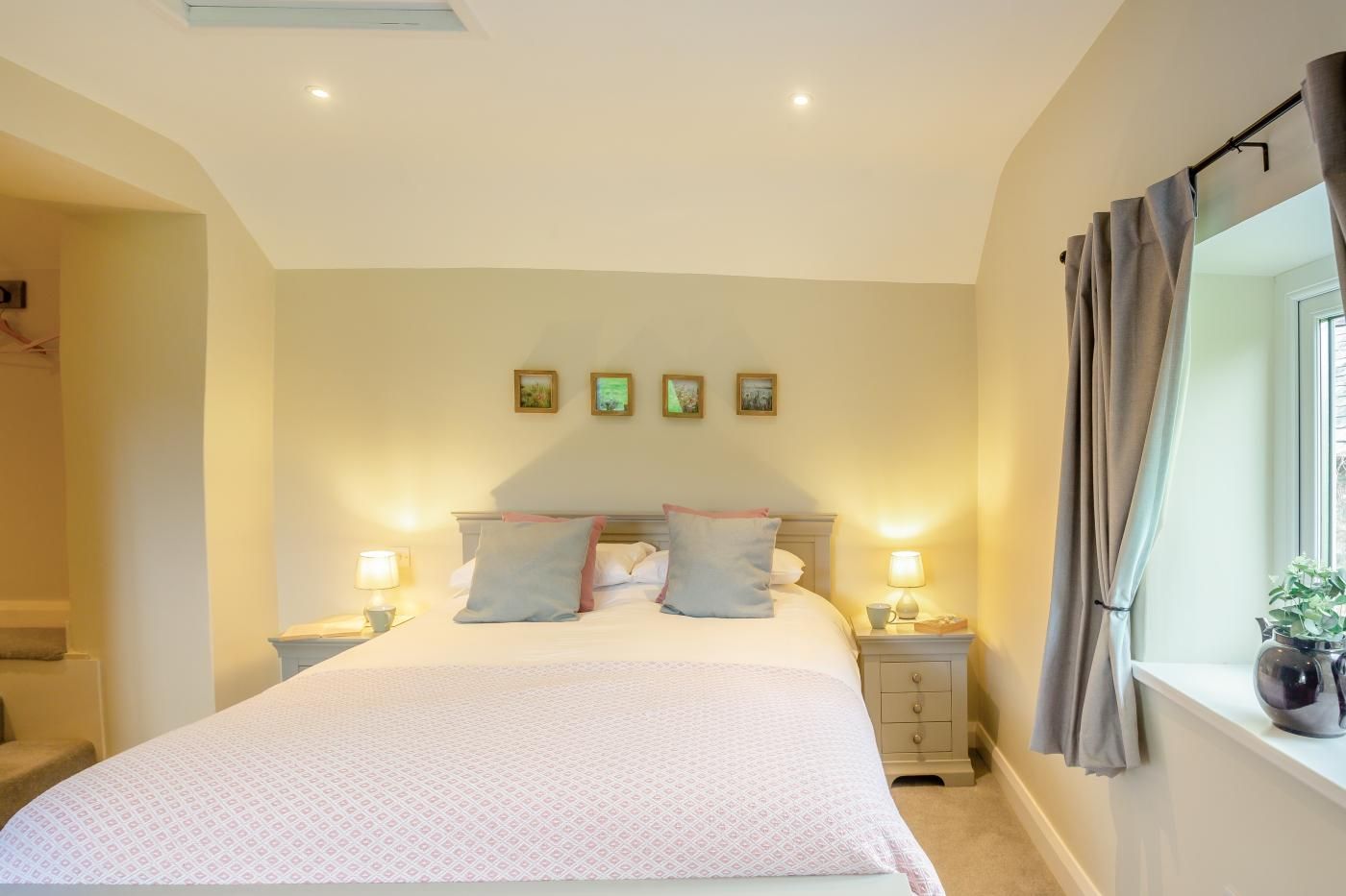 Une chambre à coucher avec un grand lit, deux tables de chevet avec des lampes, une fenêtre avec des rideaux et des tableaux accrochés au mur.
