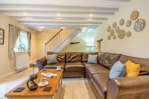 A living room with a brown leather sofa, a wooden coffee table, and a staircase in the background. - 2 Bed in Abergele (oc-88974) (Llanfair Talhaiarn)