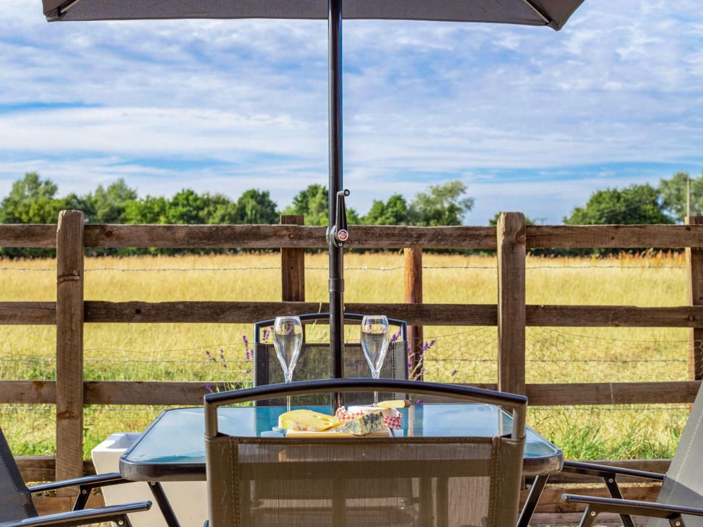 Een terras met een eettafel voor twee personen, een houten hek en uitzicht op een veld.