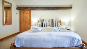 Quarto com cama de madeira, duas luminárias de cabeceira, um espelho e uma porta de madeira.