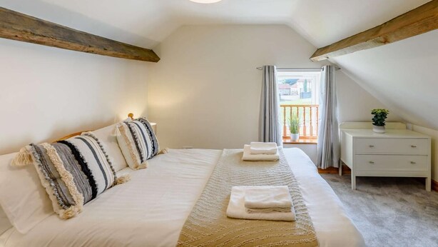 Quarto com cama, mesas de cabeceira, luminária pendente, janela com cortinas e vista exterior.