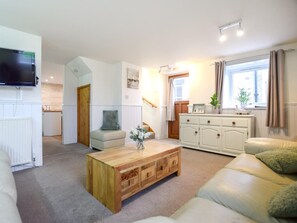 Ein modernes Wohnzimmer mit Flachbildfernseher, Couch, Holztisch, Schrank und einer Treppe zu einem weiteren Raum.