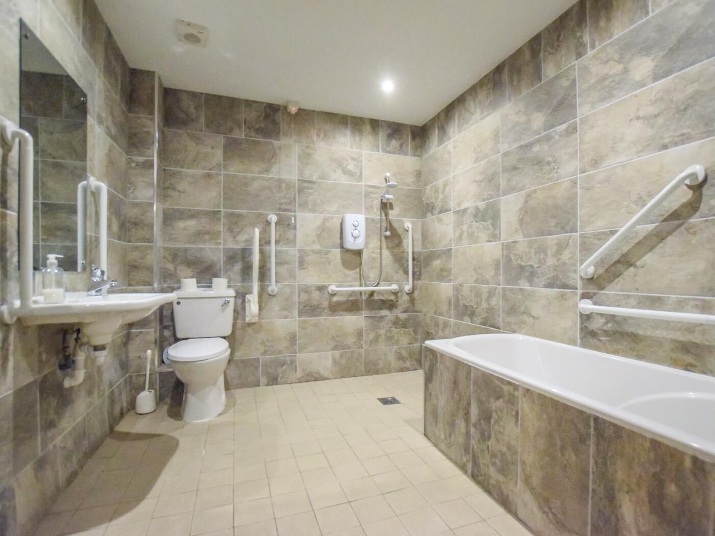 A bathroom with a toilet, sink, bathtub, and handrails.