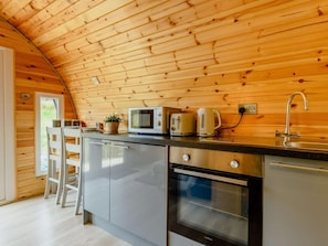 A compact kitchen with wooden walls, a microwave, a kettle, a sink, and a dishwasher.