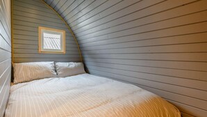 A bedroom with a curved ceiling, a bed with striped bedding, and a framed picture on the wall.