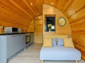 A compact, wooden cabin with a kitchenette, a bed with pillows, and a circular window.