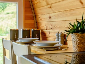 A wooden interior with a dining table set for two, featuring a coffee and sugar dispenser, salt and pepper shakers, and a potted plant.
