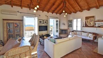 Uma sala de estar espaçosa com teto de madeira, televisão, lareira e vista para o exterior.