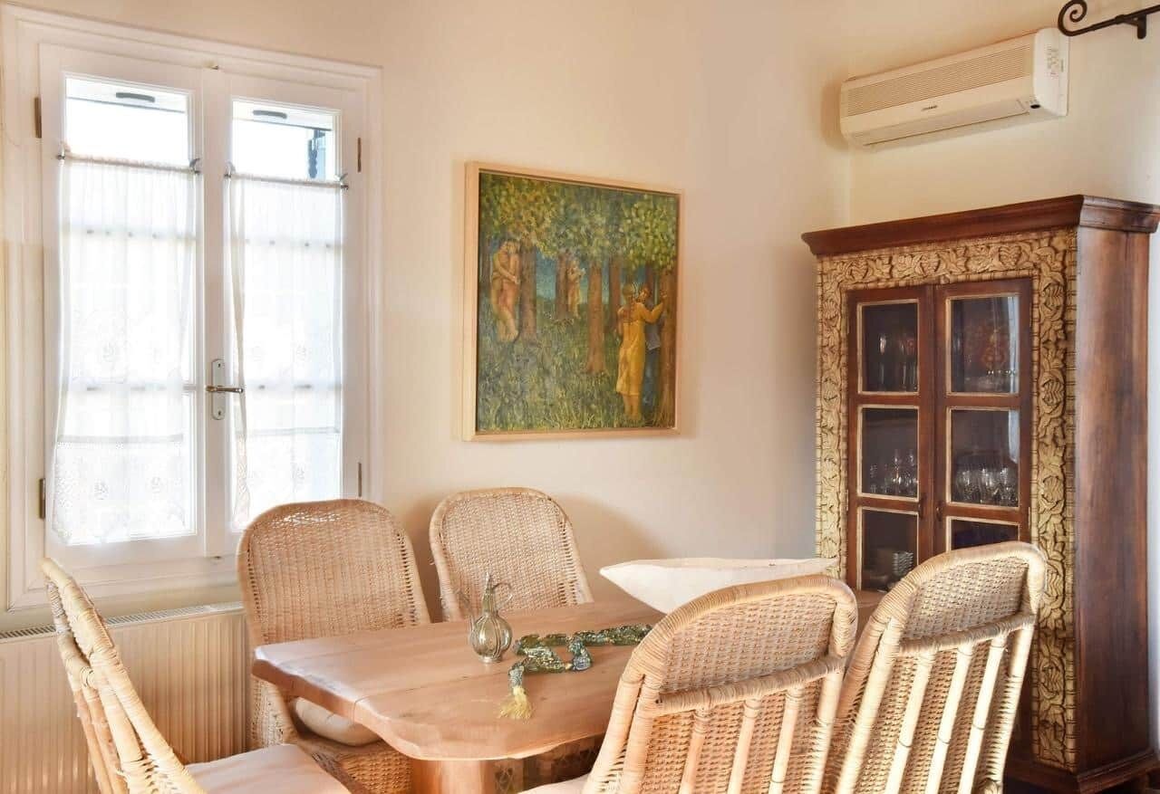 Un comedor con sillas de mimbre, una mesa de madera y un armario con puertas de cristal.