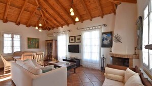 A spacious living room with a high wooden ceiling, a fireplace, a television, and a comfortable seating area. - Casa di Spetses - Luxury villa accommodation (Spetses)