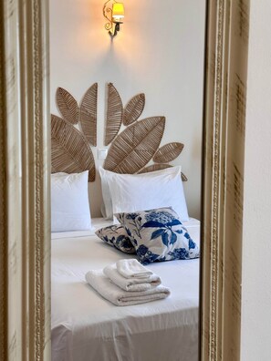 A neatly made bed with white linens, a decorative wall headboard, and a wall-mounted light fixture.