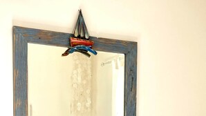 A mirror with a rustic frame, a bed with white bedding, a small wooden nightstand, and a hanging decorative item. - Casa di Spetses - Luxury villa accommodation (Spetses)