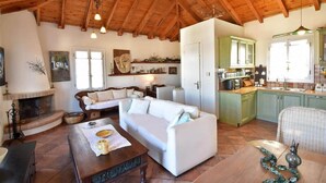 A cozy living room with a fireplace, a sofa, a dining table, and a kitchen area. - Casa di Spetses - Luxury villa accommodation (Spetses)