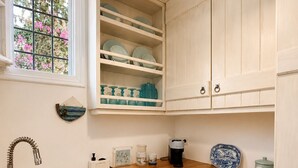 A kitchen with white cabinetry, a wooden countertop, a stainless steel sink, and a window with pink flowers outside. - Casa di Spetses - Luxury villa accommodation (Spetses)