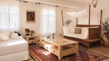 A bedroom with a four-poster bed, a daybed, a sofa, a wooden coffee table, and a patterned rug.