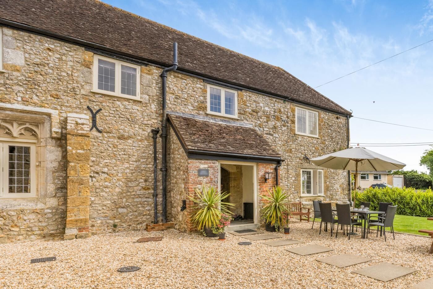 A stone building with a tiled roof, a covered entrance, and a patio area with outdoor furniture.