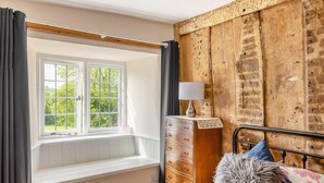 Une chambre avec une fenêtre, une commode, une lampe et un lit avec des oreillers.
