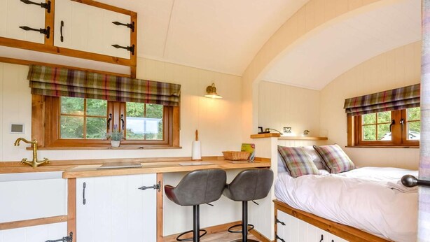 Una habitación acogedora con cama, escritorio, dos sillas, ventana con cortinas y una pequeña cocina.