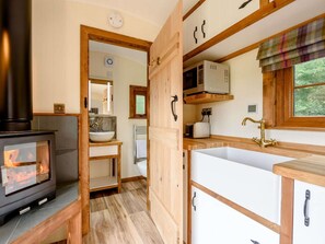 A compact kitchen with a wood-burning stove, a sink, and a window with a view. - 1 Bed in Pembroke (oc-89099) (Lamphey)